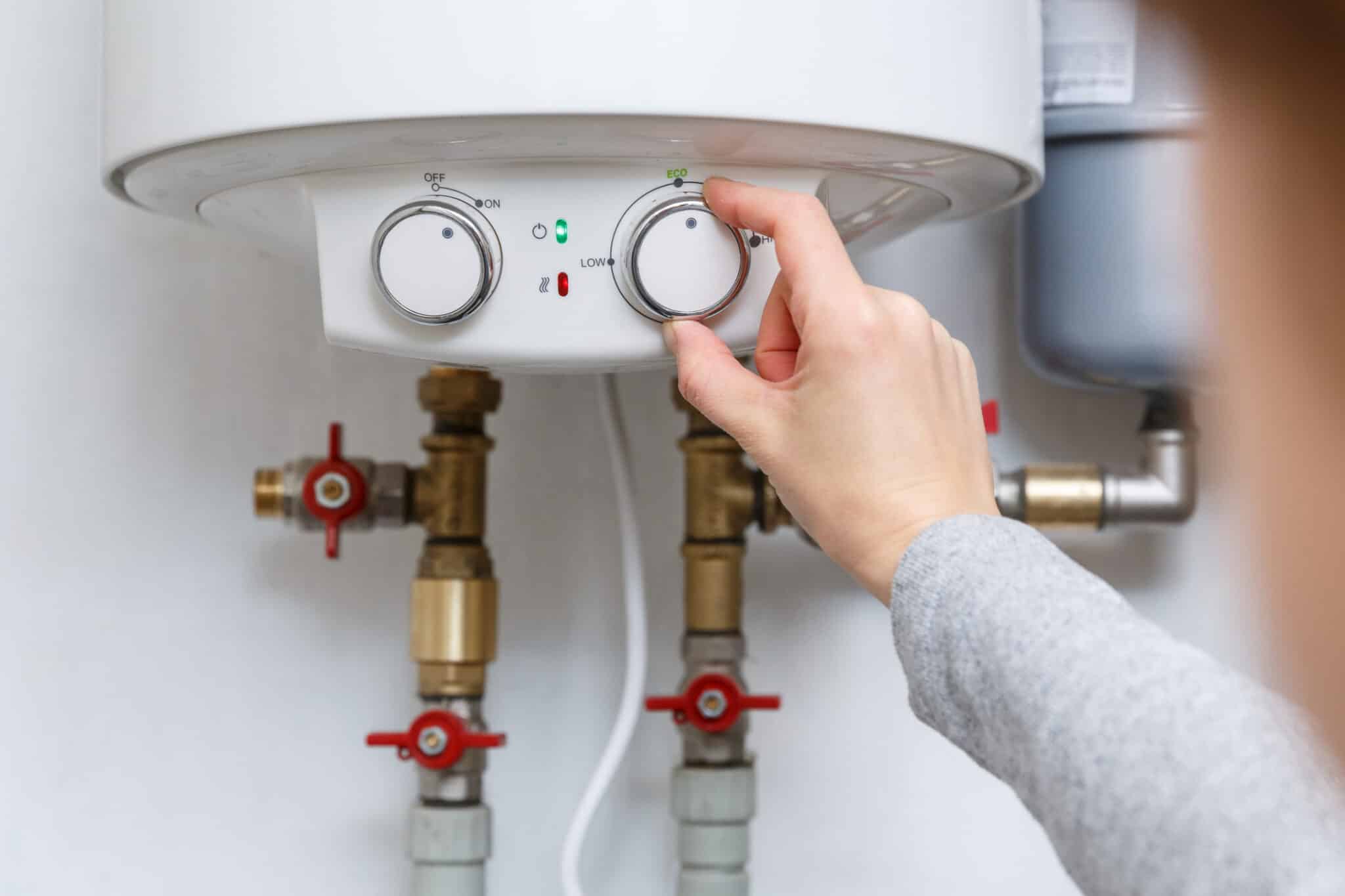 A hand adjusting the temperature of a water heater to optimize utility savings, comfort, and efficiency.